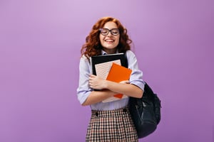 curly-girl-eyeglasses-holds-notebooks-purple-wall